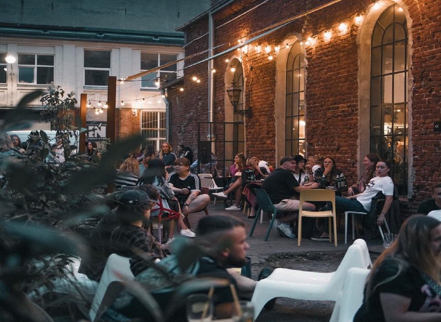 Ludzie siedzący przed lokalem przy stolikach wieczorem