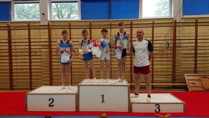 Chłopcy w wieku szkolnym wraz z trenerem pozują na podium trzymając medale i dyplomy. - Chłopcy w wieku szkolnym wraz z trenerem pozują na podium trzymając medale i dyplomy.