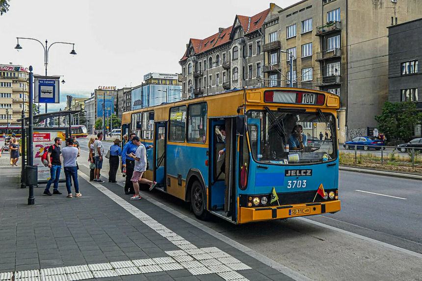 Na zdjęciu widać zabytkowy niebiesko-żółty autobus linii turystycznej "100" stojący na przystanku. Na przystanku znajdują się ludzie, którzy wsiadają do autobusu.