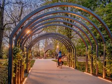 Rowerzysta jadący przez łuki oplecione roślinnością - wieczorne ciepłe oświetlenie w Parku Staromiejskim