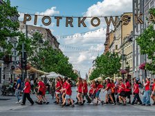 Na zdjęciu grupa młodzieży przechodząca przez ulicę po przejściu dla pieszych. Nad ich głowami na linie zawieszony napis PIOTRKOWSKA.