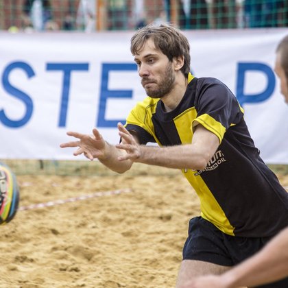 Rugby plażowe. Zawodnik ma wyciągnięte ręce do przodu szykując się do złapania piłki która zmierza w jego kierunku.