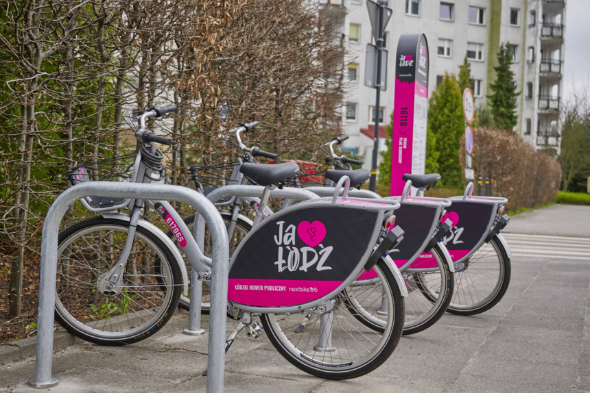 Na zdjęciu widać stojak na rowery, w którym umieszczone są srebrne rowery miejskie z różowymi elementami ozdobnymi na tylnym kole.