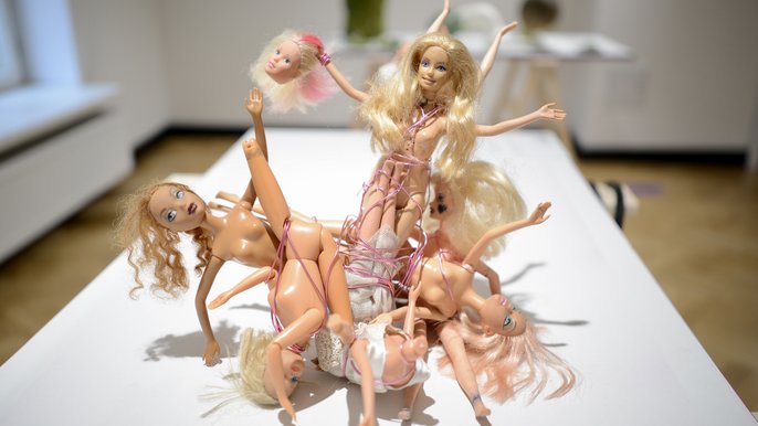  - Na zdjęciu kilka różnych nagich lalek typu Barbie złączonych ze sobą sznurkiem w wygiętych pozach.