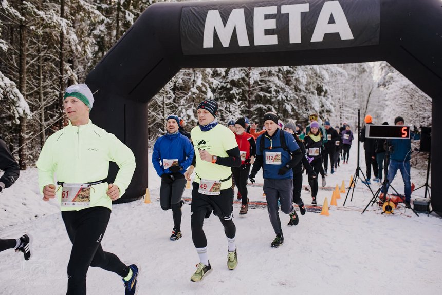 Grupa ludzi wbiega na metę po śniegu na tle zimowych drzew. Na górze zdjęcia napis Meta (biały na czarnym tle)