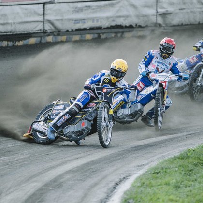 Żużel. Trzech zawodników wchodzi w wiraż. Motory pochylone są w prawą stronę.