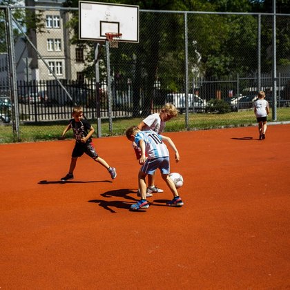 Chłopcy grający w koszykówkę na boisku typu Orlik. Chłopiec na pierwszym planie kozłuje piłkę.