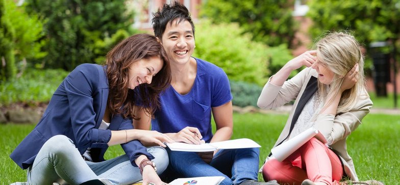 Roześmiana grupa studentów wypoczywa na trawie.