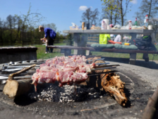 Na pierwszym planie widać mięsne szaszłyki na palenisku grillowym, na drugim planie widać stół bogato zastawiony jedzeniem i piciem na Stawach Stefańskiego