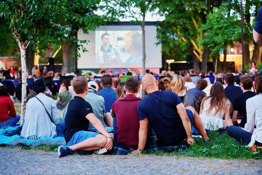 Ludzie siedzący na trawie podczas oglądania kina plenerowego na Księżym Młynie