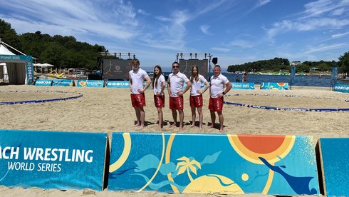 na zdjęciu zawodnicy Master Łódź na arenie do beach wrestlingu wraz z trenerami ubrani w narodowe barwy