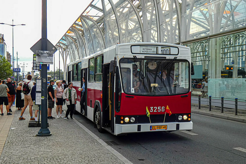 Na zdjęciu widać zabytkowy biało-czerwony autobus linii turystycznej "100" stojący na przystanku w centrum Łodzi. Na przystanku znajdują się ludzie, którzy wsiadają do autobusu.