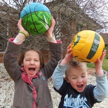 Dwójka dzieci radośnie krzyczy unosząc piłki nad głowami.