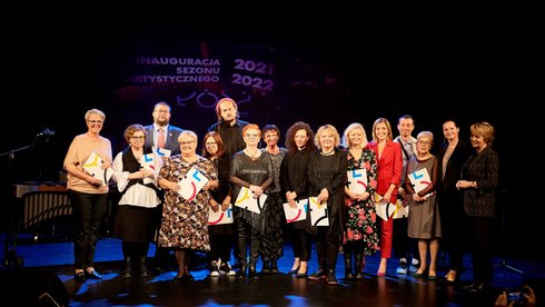 Na scenie teatralnej stoi grupa ludzi. W dłoniach trzymają listy gratulacyjne. Są to laureaci nagród. 