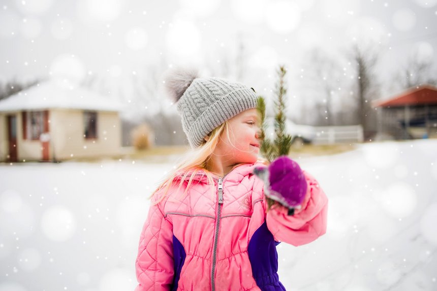 Uśmiechnięta dziewczynka trzyma gałązkę świerku. W tle zimowy krajobraz.
