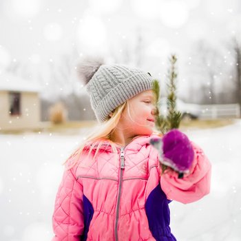 Uśmiechnięta dziewczynka trzyma gałązkę świerku. W tle zimowy krajobraz.