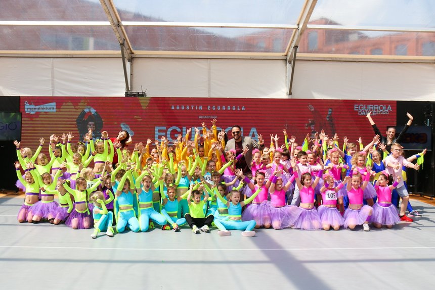 Ogromna grupa dzieci przebrana w kolorowe stroje do tańca pozuje z uśmiechem.