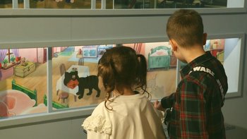  - Dziewczynka z chłopcem w muzeum oglądają obrazki przez szybę