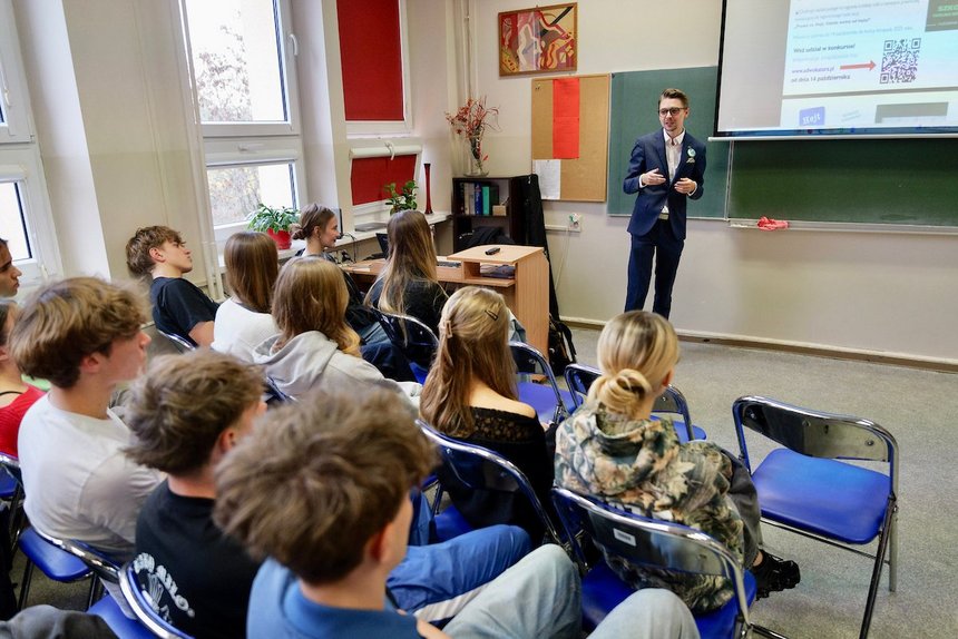 Klasa lekcyjna. Uczniowie przysłuchują się wykładowi prowadzonemu przez młodego adwokata. Tablicę przykrywa ekran z wyświetloną prezentacją z napisem "Hejt"