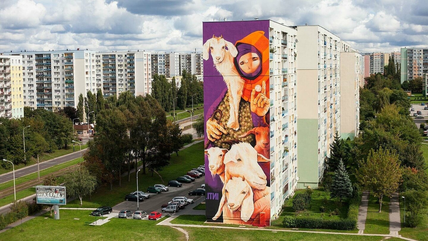 Mural z wizerunkiem kolorowej postaci i dwóch kóz na szczycie