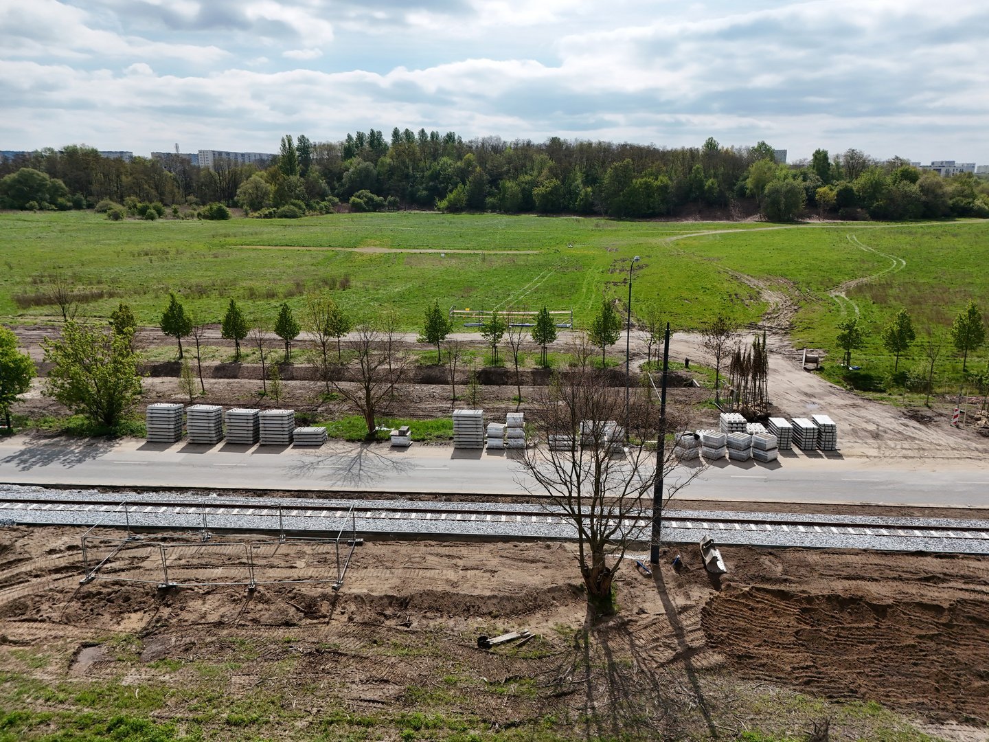 Widok z góry na fragment trasy. Torowisko i ulica biegną wśród pól. Wzdłuż ulicy rosną drzewa. 