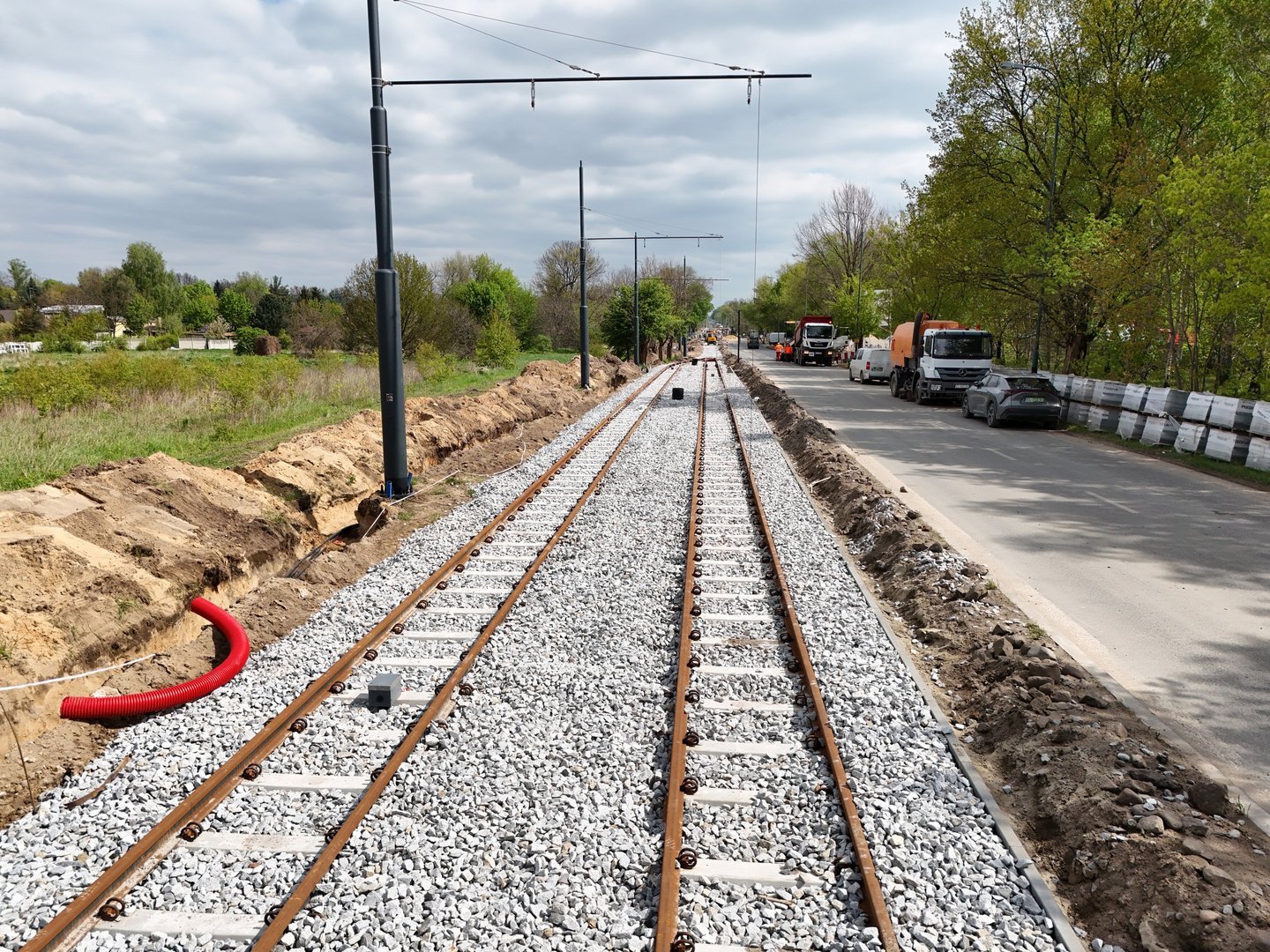 Nowe torowisko. Dwie linie torów po prawej stronie ulica. Torowisko wysypane kamieniami. Po lewej stronie słupy trakcyjne doprowadzające prąd dla tramwajów. 