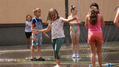 Dzieci bawiące się na dworze zraszaczami wodnymi w letni dzień